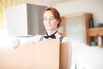 Junge Frau mit weißer Bluse, Hosenträger, Fliege und Papiertüte zu Hause