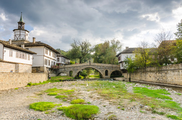 Old bridge (also called hunchback bridge) on the Trevnenska river and the clock tower in town of Tryavna