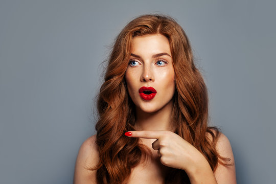 Surprised girl pointing. Excited redhead woman pointing on blue background with copy space