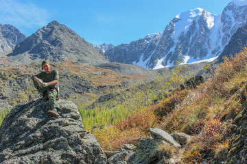 Man-tourist sitting on a stone on a background of snow-white mountain peaks
