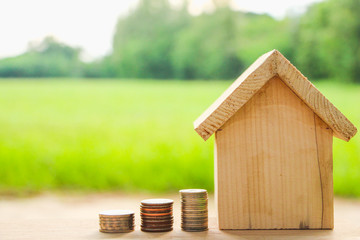 Miniature wood house with coin money on wood table green background.