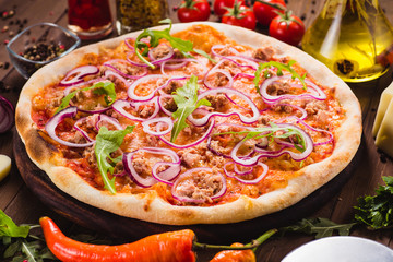 Italian pizza with chicken, onions and rucola leaves on a dark wooden background with ingredients...