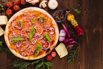Italian pizza with chicken, onions and rucola leaves on a dark wooden background with ingredients around (close top view)