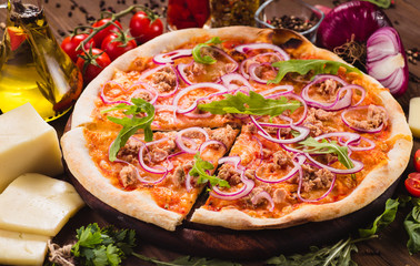 Italian pizza with chicken, onions and rucola leaves on a dark wooden background with ingredients around (close). Cut one piece