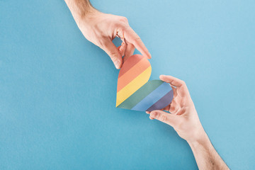 cropped view of men holding rainbow colored paper heart on blue background, lgbt concept