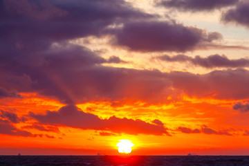 Obraz premium bright orange sun in a cloudy sky over the sea during sunset