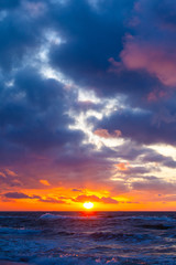 Obraz premium bright orange sun in a cloudy sky over the sea during sunset