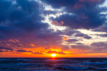 Fototapeta premium bright orange sun in a cloudy sky over the sea during sunset