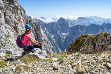 Naklejka na ściany i meble Young girl enjoying the views from a peak in Julian Alps, Triglav National Park, Slovenia, during a break on a via ferrata route, on a hot, bright, Summer day