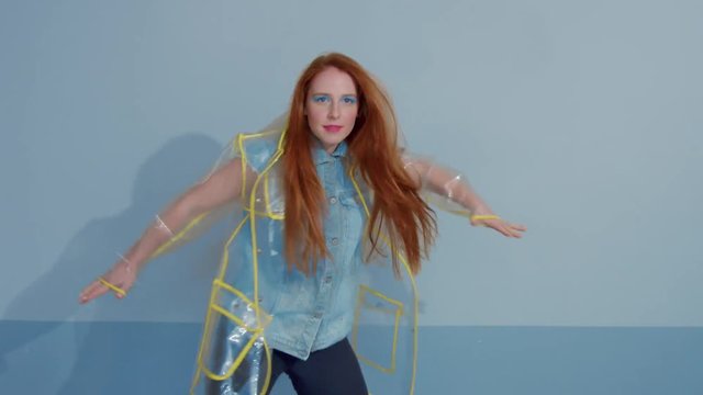 ginger hair woman in transparent raincoat with pop art bright makeup dancing strange dancing