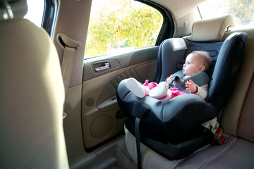 Adorable baby girl sitting and looking outside of a cars window