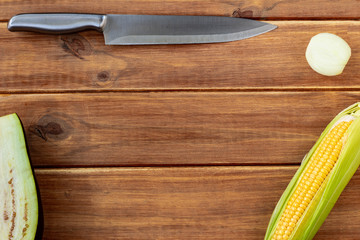 A silver metal knife next to some vegetables on a rustic wooden table. Free space for writing. Top view of the table