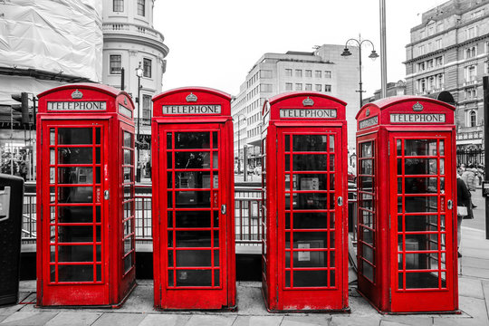 A traditional British red telephone boxes are standing on the street. Booth is isolated in a black and white picture. 