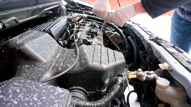The car will not start, it's cold outside. A man unscrews a car engine spark plug. Side view.