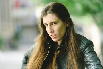 Young model woman with long straight hair wearing leather jacket posing carefree and casual on the street.