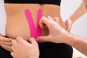 Man's Hand Applying Physio Tape On Woman Lower Back