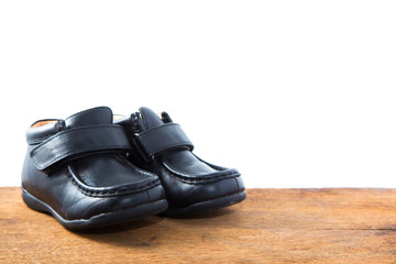 Baby black leather shoes on wood and white background