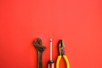 Screwdriver, rusty adjustable spanner and pliers shot on a plain isolated red background as...