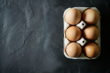 Top view of chicken eggs in cardboard box on slate with text space