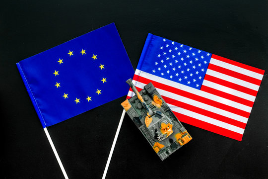 War, confrontation concept. European Union, USA. Tanks toy near european and american flag on black background top view