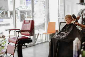 Little boy sitting in armchair in barbershop and having new haircut