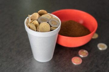 Styrofoam cup full of coins with red bowl of instant coffee