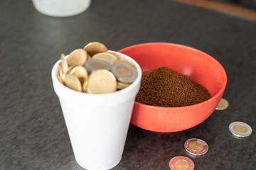 Styrofoam cup full of coins with red bowl of instant coffee