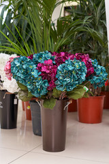 Artificial flowers are hydrangea turquoise and crimson. Artificial flowers stand on a tiled floor in a vase