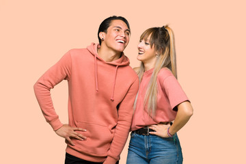 Young couple posing with arms at hip and laughing over pink background