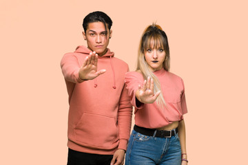 Young couple making stop gesture denying a situation that thinks wrong over pink background