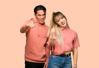 Young couple frustrated by a bad situation and pointing to the front over pink background