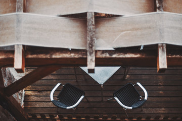 View from above on a street cafe under the canopy with two curved armchairs and an empty metal table on the wooden floor