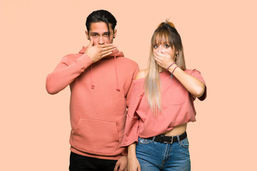 Young couple covering mouth with hands for saying something inappropriate over pink background