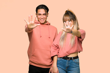 Young couple counting five with fingers over pink background