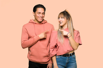 Young couple pointing to the side to present a product over pink background