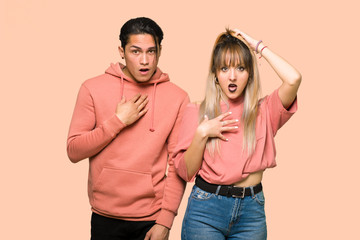 Young couple surprised and shocked while looking right over pink background