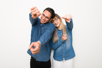 Young couple with glasses points finger at you while smiling