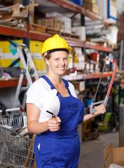 Female  in uniform and helmet holding saw and standing near racks in build store