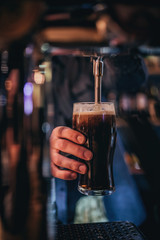 The man behind the bar pours beer holding a mug in his hand