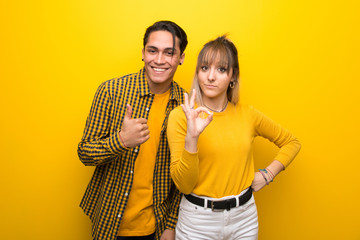 Obraz premium Young couple over vibrant yellow background showing ok sign with and giving a thumb up gesture