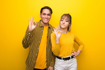 Young couple over vibrant yellow background showing an ok sign with fingers