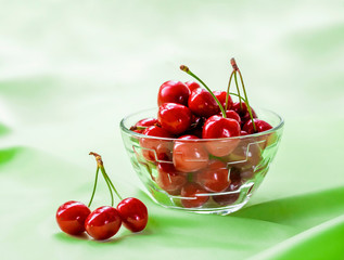 Juicy ripe sweet cherries in glass bowl on gently green cloth background