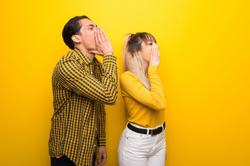 Young couple over vibrant yellow background shouting with mouth wide open to the lateral