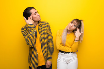 Young couple over vibrant yellow background with problems making suicide gesture