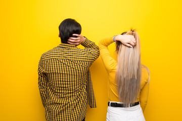 Young couple over vibrant yellow background on back position looking back while scratching head