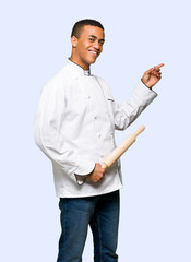 Young afro american chef man pointing finger to the side in lateral position on isolated background