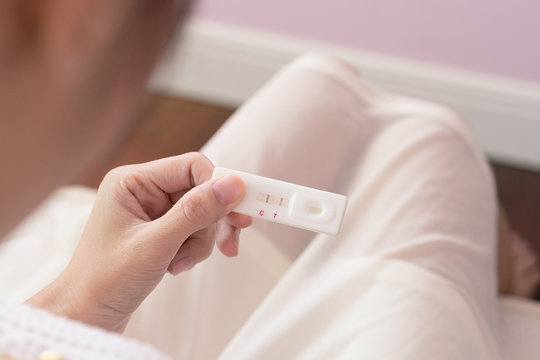 Pregnant asia woman in white dress looking at pregnancy test strip with happy and excited, close up of pregnancy test strip