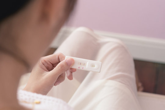Pregnant asia woman in white dress looking at pregnancy test strip with happy and excited, close up of pregnancy test strip