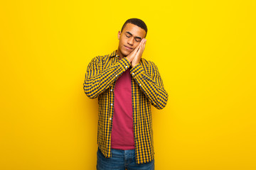 Young afro american man on yellow background making sleep gesture in dorable expression