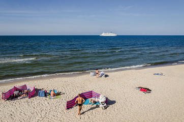 Fototapeta na wymiar REST ON THE SEA BEACH - People on golden sand and a cruise passenger ship on the sea